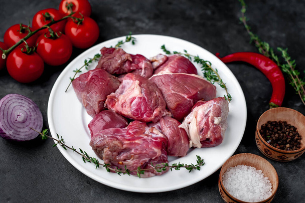 Świeże plasterki? ? surowe mięso wołowe w białej misce na kamiennym tle z pomidorami i przyprawami - Zdjęcie, obraz