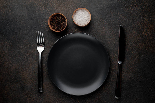 plato negro con especias con tenedor y cuchillo sobre un fondo de piedra
 - Foto, imagen