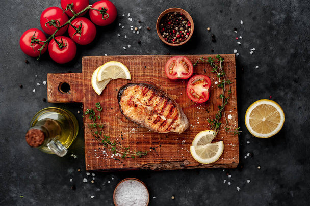 Grilled salmon steak with spices, lemon and tomatoes on a stone background. - Fotoğraf, Görsel
