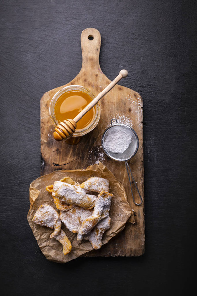 Composition of faworki - angel wings, powdered sugar and honey on the cutting board, on the stony countertop. Sweet, carnival pastries. - Fotoğraf, Görsel