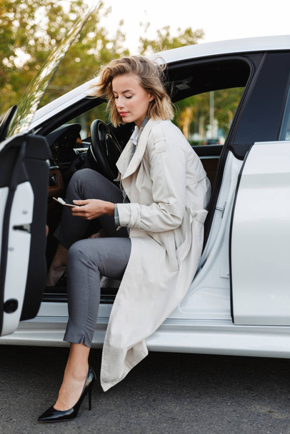 Image of beautiful businesslike woman sitting in car and using c - Foto, imagen