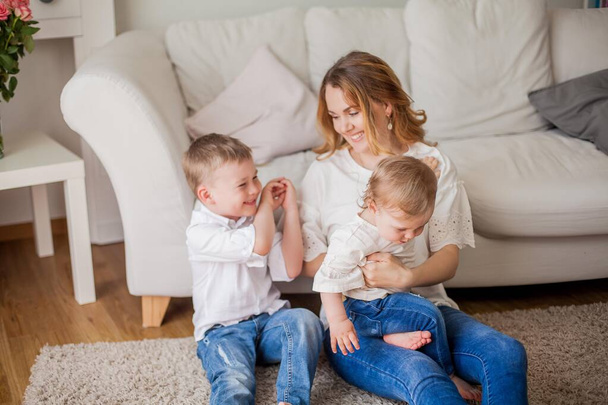 Beautiful young mother, little son, little daughter are sitting on the sofa at home. Mothers Day. A happy family. Cozy. - Foto, immagini