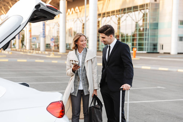 Image of businesslike man and woman standing with luggage by car - Fotoğraf, Görsel