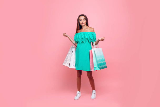 Portrait of a stylish smiling beautiful woman in an off-the-shoulder dress holding bags on an isolated pink background - Fotó, kép