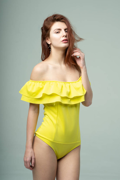 young beautiful girl posing in studio, standing in a yellow bathing suit - Фото, изображение