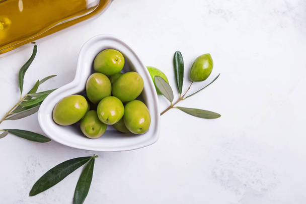 Heart shaped bowl full of green olives on a white table, - Φωτογραφία, εικόνα