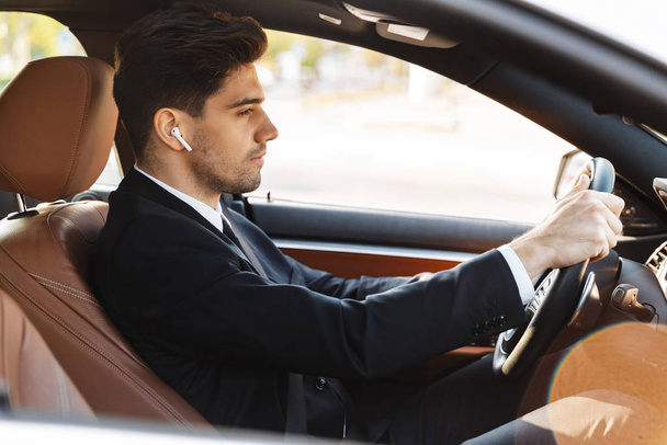 Fénykép a fókuszált fiatal üzletember használó fülhallgató vezetés közben autó - Fotó, kép