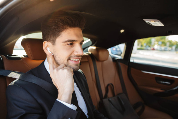 Image of young caucasian businesslike man in suit riding in car - Foto, afbeelding