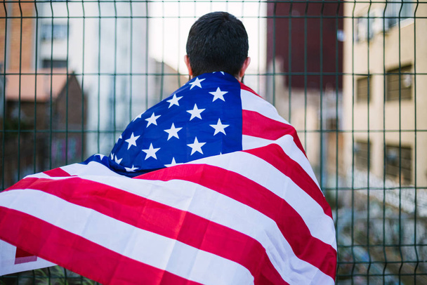 Młody chłopiec z amerykańską flagą wiszącą na plecach. Koncepcja Dnia Niepodległości Stanów Zjednoczonych - Zdjęcie, obraz