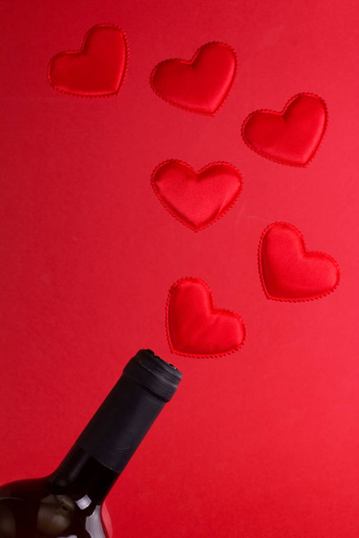 Bottle of wine with hearts on red background. Levitation. Top view.  - Foto, afbeelding