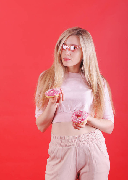 Улыбающаяся белая женщина с розовыми пончиками позирует на красном фоне в студии
. - Фото, изображение
