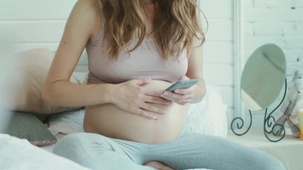 Nahaufnahme unerkannt Bauch Mutter tippt Nachricht auf Handy im Schlafzimmer. - Filmmaterial, Video