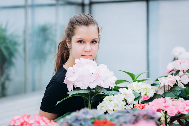 joven hermosa chica de pelo largo en un invernadero con flores de hortensias de primavera
 - Foto, Imagen