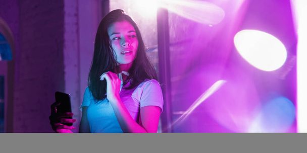 Cinematic portrait of handsome young woman in neon lighted interior - 写真・画像