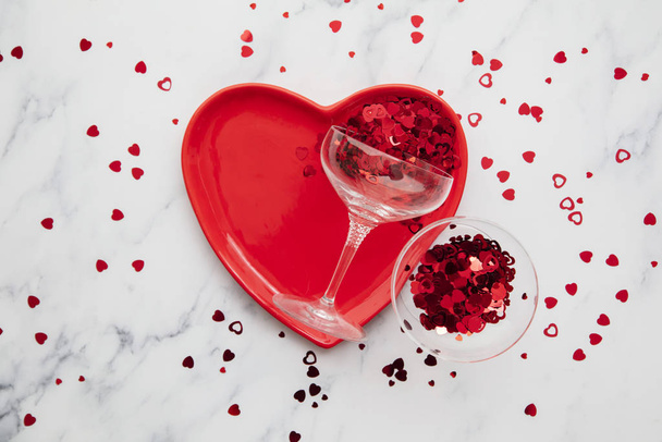 Valentines dinner background. Red heart plate with champagne glass and confetti - Photo, Image