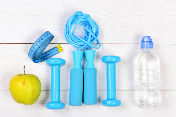 Barbells, jump rope, bottle, apple and centimeter on wooden background - 写真・画像