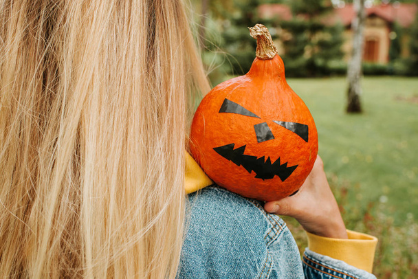 Halloween pumpkin. Woman holding a scary face pumpkin. Happy Halloween party holiday. Celebrate annual in October 31. Autumn season. Fall color, orange and yellow. Trick or treat. Young girl outdoors - Photo, image