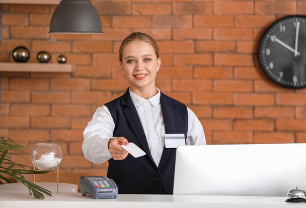 Jonge vrouwelijke receptioniste met kaart aan balie in hotel - Foto, afbeelding