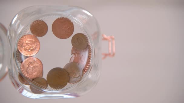 A worm's eye view of someone dropping pennies into a glass jar - Footage, Video