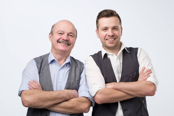 Two caucasian men, a mature adult around 30 years and a senior standing with folded hands and smiling - Photo, Image