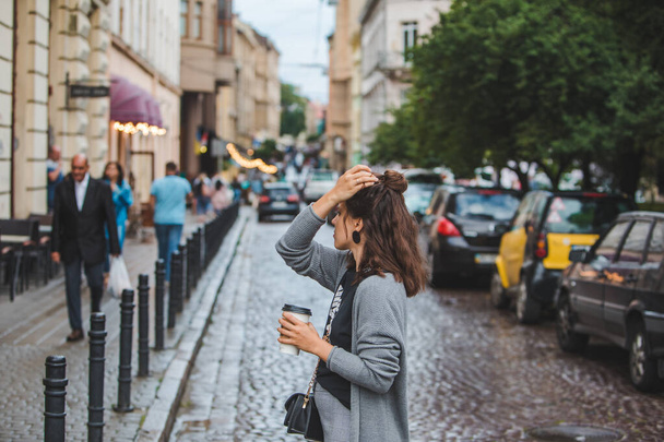 Şehir caddesinde tek kullanımlık fincandan kahve içen genç ve güzel bir kadın. - Fotoğraf, Görsel