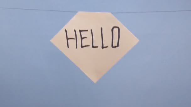 Een man hangt een wit vel papier met een zwarte inscriptie hallo op een blauwe achtergrond - Video