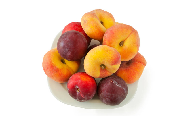 New variety of flat peaches and plums lying on white dish against a white background - Foto, Imagem