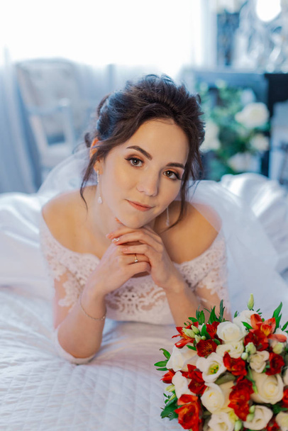 Beautiful happy bride on the bed with a wedding bouquet. - Zdjęcie, obraz