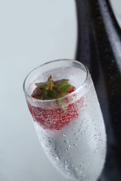 Closeup of a chilled glass of champagne with a strawberry floating in it - Foto, immagini