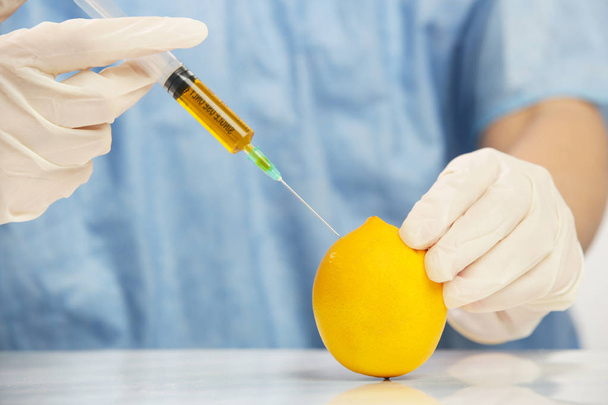 Fechar a agulha injetada no limão, conceito de alimento geneticamente modificado
 - Foto, Imagem