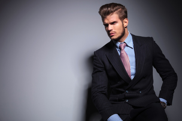 seated young fashion model in suit looks away - Photo, Image