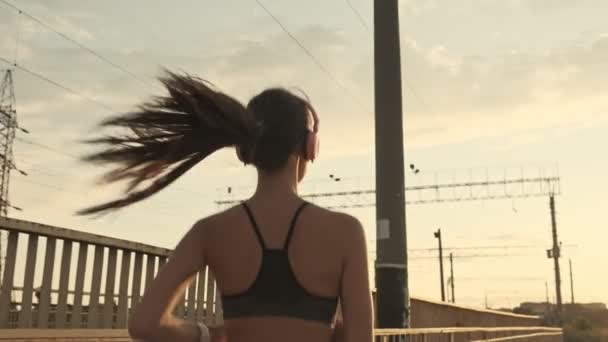 Back view of pretty asian sports woman in headphones listening music and running outdoors - Materiał filmowy, wideo