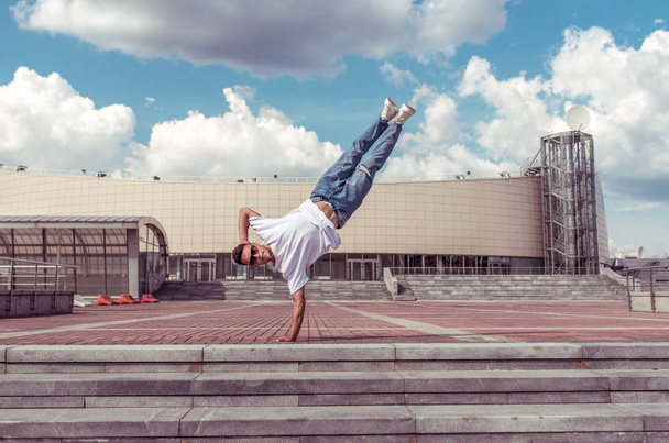 man standing on one arm, young guy dancer, summer city, dancing street dances, break of movement, modern youth style. Fashion fitness sport. Free space for copy text. Step cloud background. - Valokuva, kuva