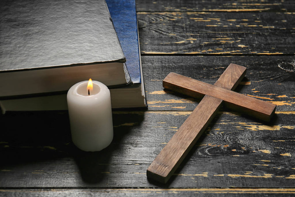Christian cross, candle and Bible on dark wooden background - Fotoğraf, Görsel