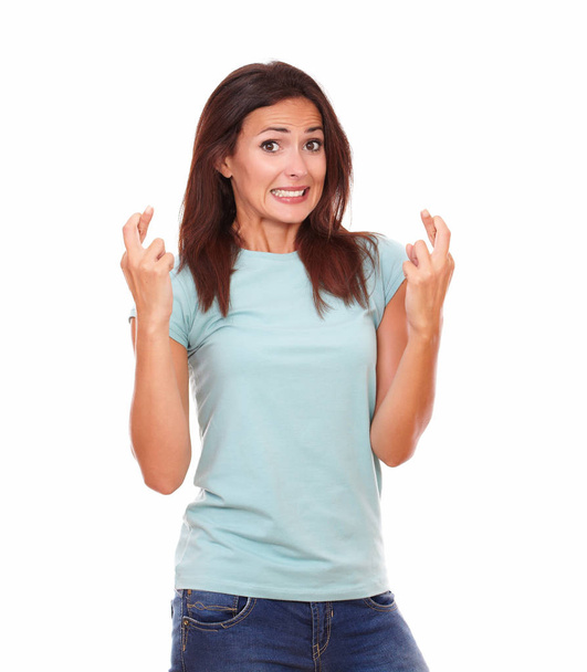 Portrait of beautiful adult lady on blue t-shirt crossing her fingers while smiling at you with funny face on isolated studio - Photo, Image