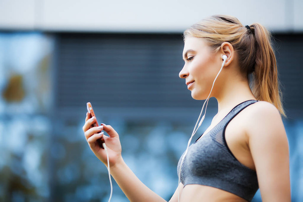 Fitness. Beautiful woman drinking water and listen to music after running - Foto, afbeelding