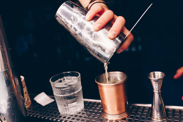 Μπάρμαν ρίχνει χρησιμοποιώντας σουρωτήρι Λευκό υγιεινό ποτό κοκτέιλ σε έναν πάγκο μπαρ. Επαγγελματική άποψη. Μοντέρνο, κομψό αλκοολούχο ποτό. Σχεδιασμός ανθρώπων και πολυτέλεια έννοια μπαρ υπηρεσία σε νυχτερινό κέντρο διασκέδασης - Φωτογραφία, εικόνα