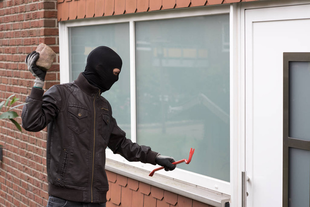 burglar breaking a window with a crowbar - Фото, зображення