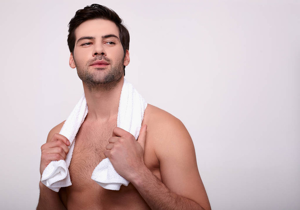 młody sexy mężczyzna pozowanie z a biały ręcznik na szary tło. - Zdjęcie, obraz