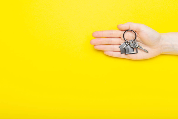 House keys with trinket in female hand on color background, top view with copy space. House key on yellow background. Minimal flat lay style with place for text. - Foto, Imagem