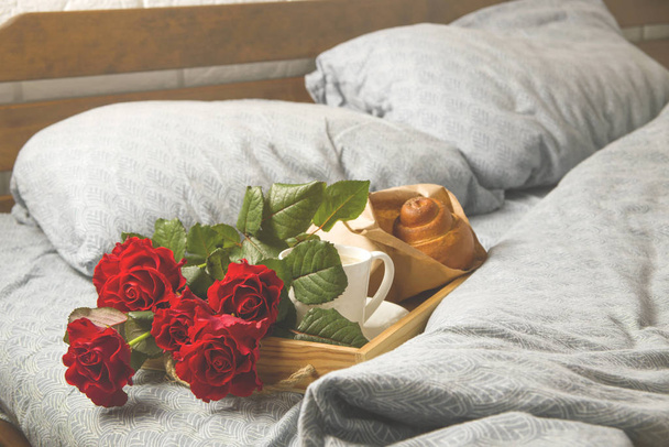 Coffee and muffins on a wooden tray. With a bouquet of flowers on the bed. - Photo, Image