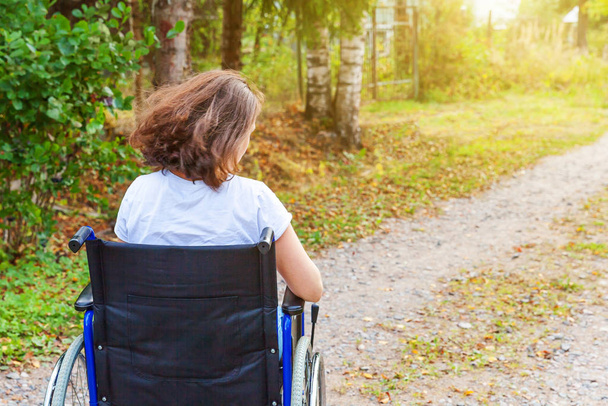 Young happy handicap woman in wheelchair on road in hospital park enjoying freedom. Paralyzed girl in invalid chair for disabled people outdoor in nature. Rehabilitation concept. - Фото, зображення