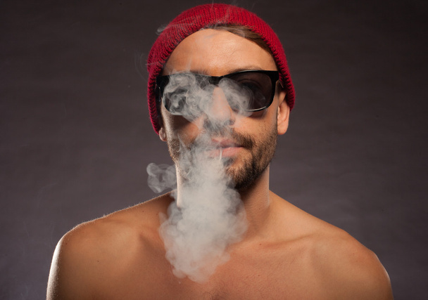 Portrait of a shirtless young man blowing smoke - Photo, Image