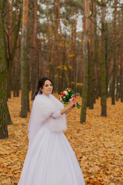 Beautiful happy bride with a wedding bouquet in the forest in autumn. - Фото, изображение