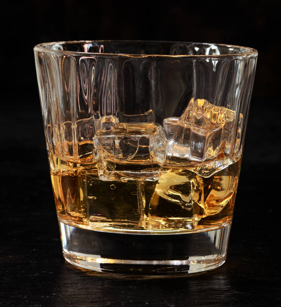 Bicchiere di whisky sulle rocce servito refrigerato a cubetti di ghiaccio per una bevanda rinfrescante al bar, da vicino vista sul nero - Foto, immagini