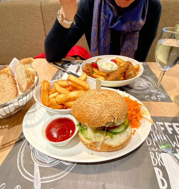Pohled shora na ženu jíst chutné ryby a hranolky vedle bohaté porce s hamburgery a hranolky - Fotografie, Obrázek