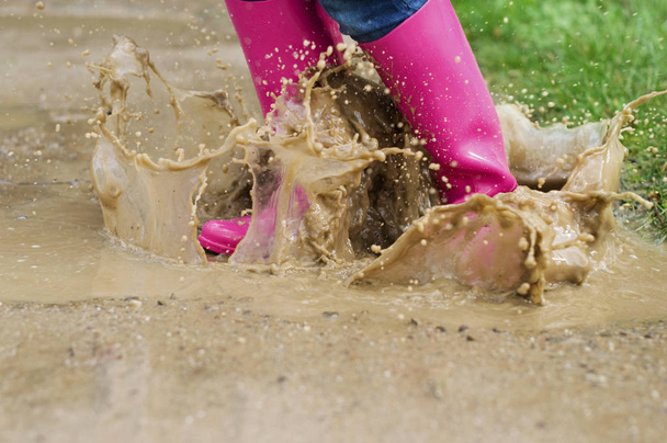 Young woman with rubber boots jumping in puddle - Fotoğraf, Görsel