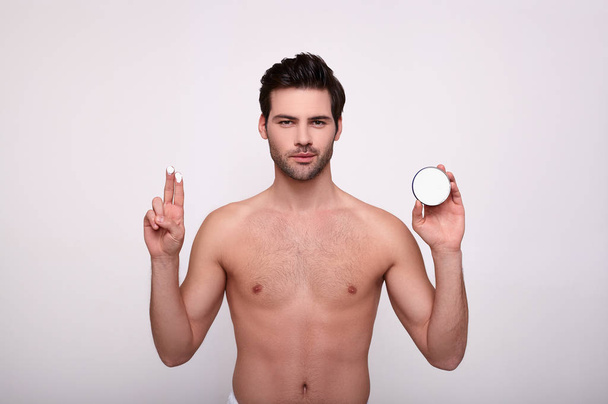 Serious male model with muscular body, applies face cream. - Fotoğraf, Görsel