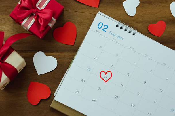 Table top view aerial image of decoration valentine's day background concept.Flat lay arrangement of calendar page of february month with essential items love heart with gift box on wooden. - Foto, Imagen