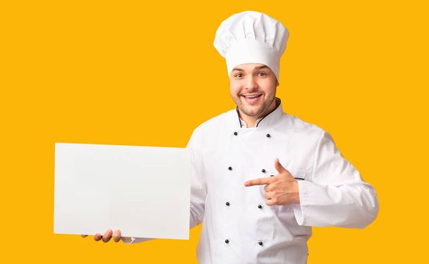 Chef Man Εμφάνιση κενής λευκό πίνακα στέκεται πάνω από κίτρινο φόντο - Φωτογραφία, εικόνα